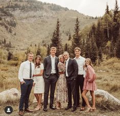 a group of people standing next to each other in front of trees and mountains on a cloudy day