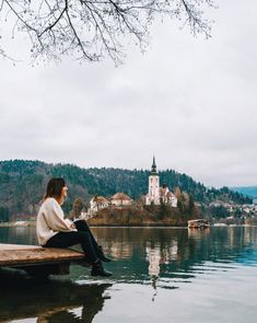 a person sitting on a bench in front of the water with a castle in the background