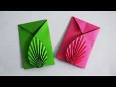 two origami pieces are sitting next to each other on a white surface, one is green and the other is pink