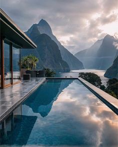 an outdoor swimming pool with mountains in the background and clouds reflecting on the glass surface