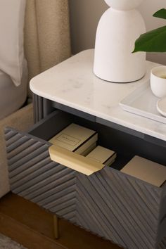 a white vase sitting on top of a table next to some books and a plant