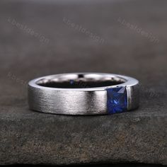 a white gold ring with a blue sapphire stone in the center on top of a rock