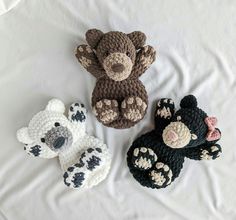 three crocheted teddy bears sitting on top of a white bed sheet, one is brown and the other is black