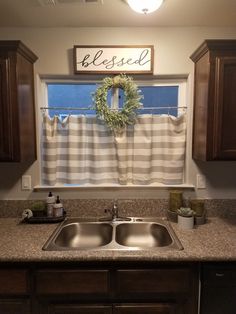 a kitchen sink under a window with a wreath on the valance and a sign above it