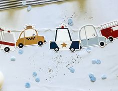 a paper cut out of cars and trucks on a white tablecloth with confetti sprinkles