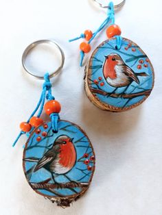 two wood slices with birds painted on them are sitting next to each other and one is hanging from a keychain