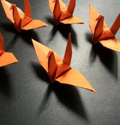 four orange origami birds sitting on top of a black table next to each other