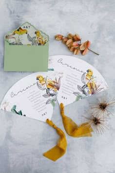 two fan shaped cards with flowers on them next to an envelope and some dried plants