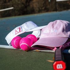 two tennis balls and a pink hat laying on the ground next to a racket