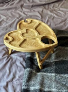 a wooden tray with three hearts on it sitting on top of a plaid bed sheet