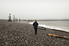 a woman standing on top of a rocky beach next to the ocean and holding onto a log