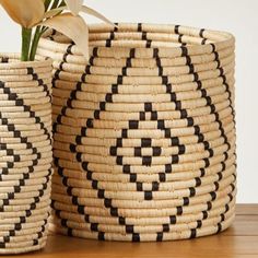 two black and white baskets sitting on top of a wooden table next to a flower