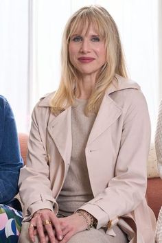 a woman sitting on top of a couch in front of a white curtain and window