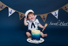 a little boy sitting on top of a cake with a spoon in his hand and wearing a sailor outfit