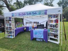 a tent set up in the middle of a field with bookshelves and tables under it