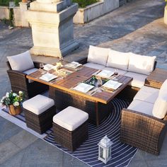 an outdoor dining table with white cushions and chairs on a rug in the middle of a courtyard