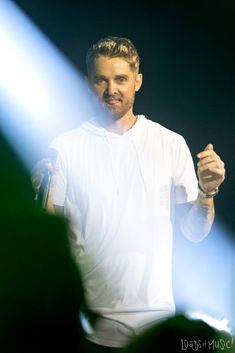 a man holding a microphone in his right hand and wearing a white shirt on stage