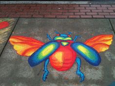 a colorful insect painted on the sidewalk next to a brick wall