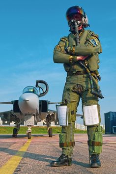 an air force pilot standing in front of a fighter jet on the tarmac with his arms crossed