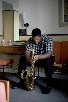 a man sitting down playing a saxophone in a room full of chairs and couches