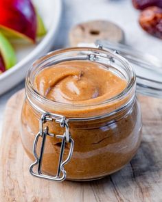 a glass jar filled with peanut butter sitting on top of a wooden cutting board next to an apple