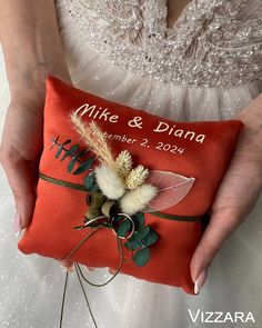 a woman holding a red pillow with a wedding date on it and flowers in the center