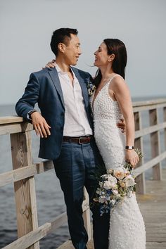 a bride and groom standing on a pier next to the ocean