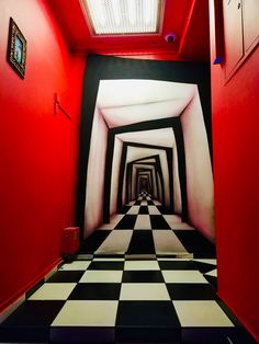 a hallway with black and white checkered flooring, red walls and framed pictures on the wall