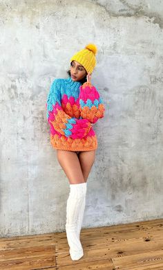 a woman in a colorful sweater and white boots poses for the camera with her hands on her hips