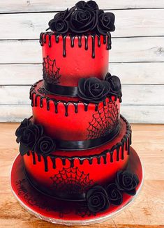 a three tiered red cake with black icing and roses on the bottom layer