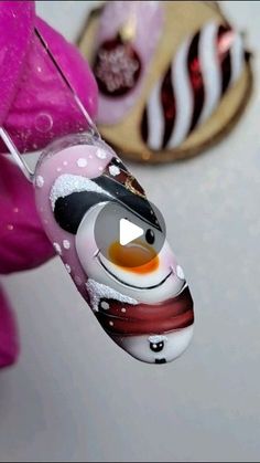 a glass ornament with a snowman on it next to a pink flower