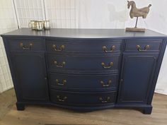 a large blue dresser with brass handles and knobs on the top, in front of a white wall