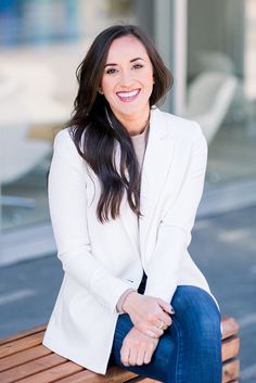 a woman sitting on top of a wooden bench smiling at the camera with her hands in her pockets