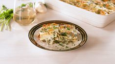 a casserole dish on a plate next to a glass of wine and some herbs