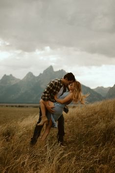 a man holding a woman in his arms while standing on top of a grass covered field