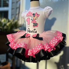 a pink and black minnie mouse birthday outfit with polka dots on the bottom, is hanging from a mannequin