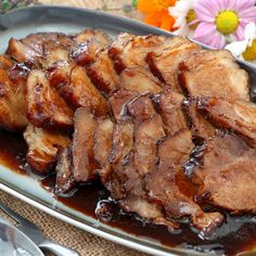 some meat is sitting on a plate with sauce and spoons next to flowers in the background