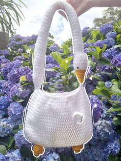 a white purse with an ice cream cone sticking out of it's handle in front of blue flowers