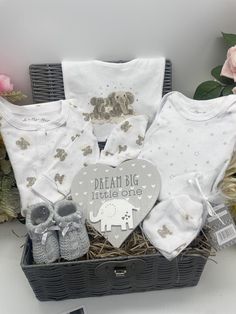 a basket filled with baby clothes next to pink roses and other items on a table