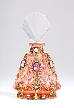 a pink glass perfume bottle with gold trimmings and jeweled decorations on the top