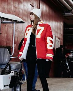 a woman standing in front of a golf cart wearing a red jacket and white hat