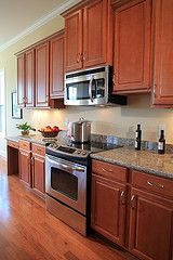 a kitchen with wooden cabinets and stainless steel appliances, along with hardwood flooring that matches the walls