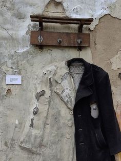 an old coat hanging on the side of a building next to a wooden hanger