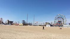 a man standing on top of a sandy beach next to a ferris wheel and roller coaster