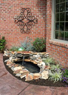 a small pond in the middle of a brick wall next to some plants and flowers