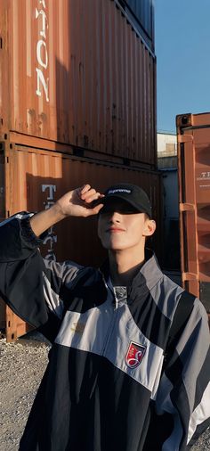 a man standing in front of some shipping containers with his hands on his head and wearing a hat