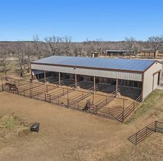 an aerial view of a horse barn in the middle of a dry grass field with trees