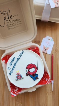 a birthday cake in a box with a spiderman design on it and a pen next to it