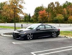 a black car parked in a parking lot next to a tree filled parking lot with lots of leaves