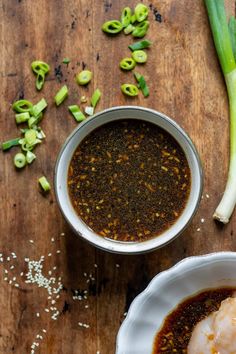 two bowls filled with sauce next to green onions and celery on a wooden table